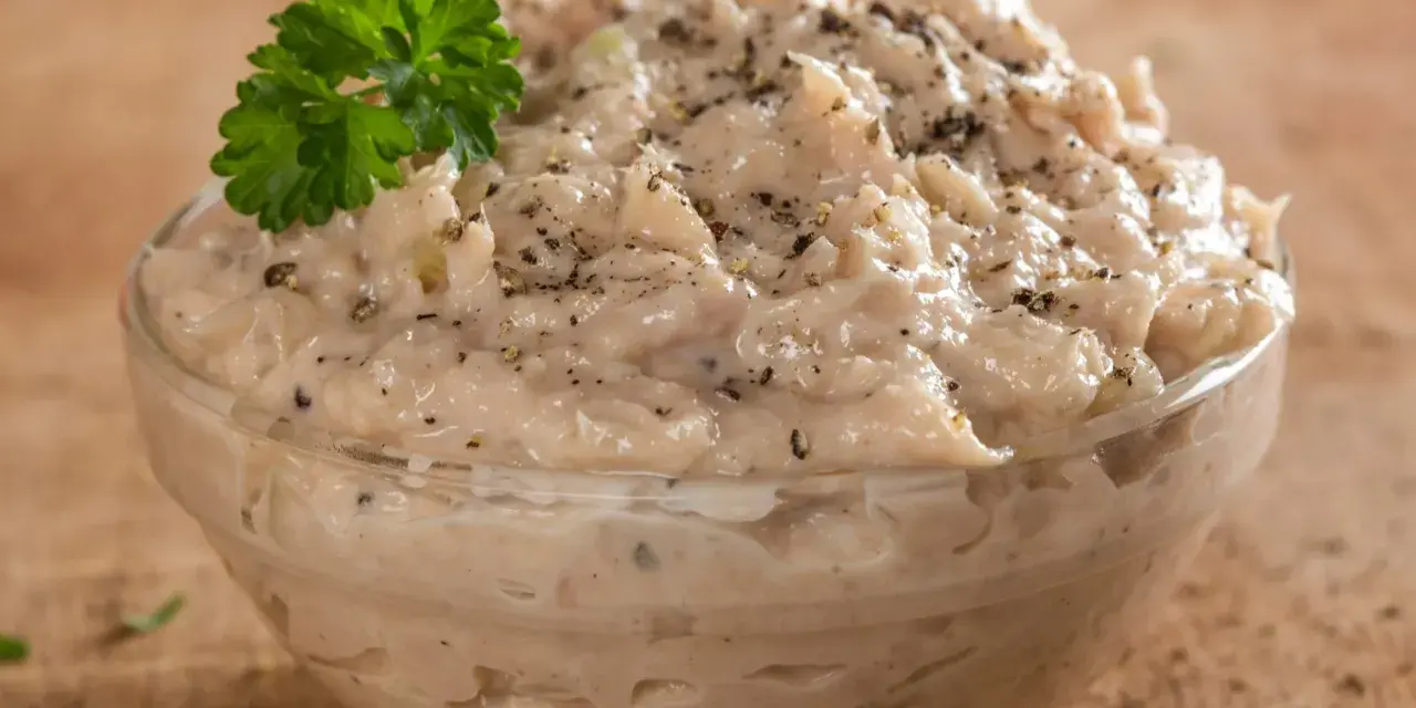 Kremowa pasta z tuńczyka, doprawiona pieprzem, w szklanej miseczce, ozdobiona gałązką natki pietruszki. Idealna na kanapki.