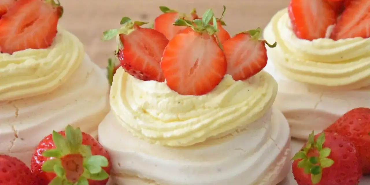 Mini torty pavlova z bitą śmietaną i świeżymi truskawkami.