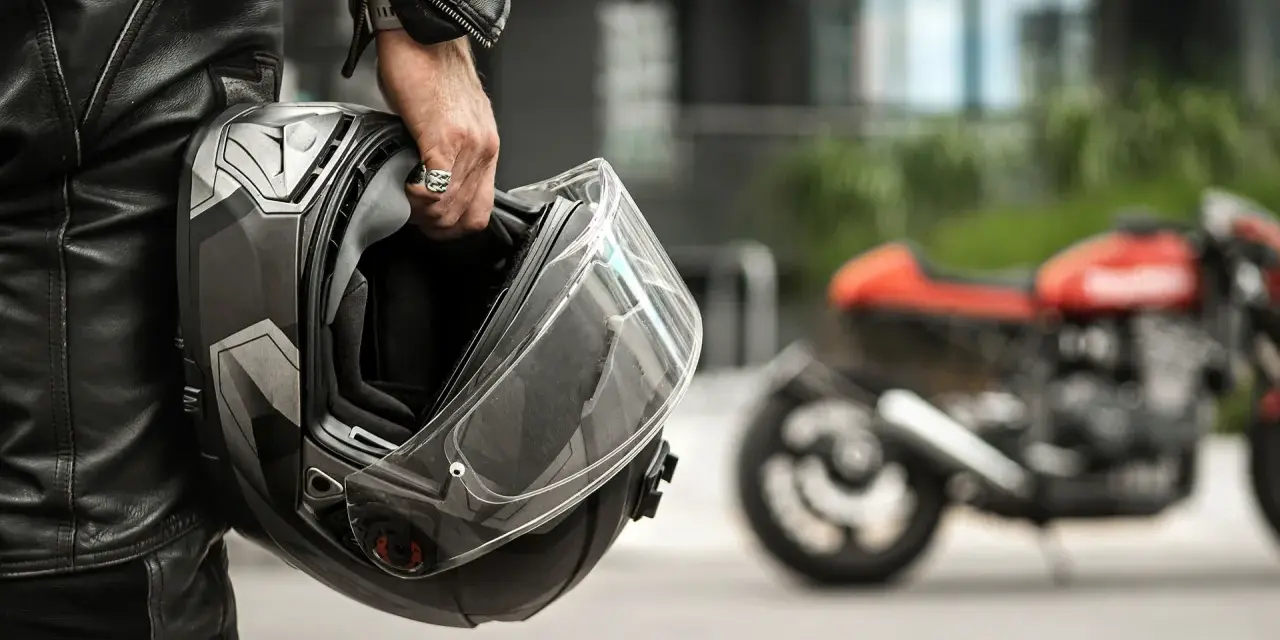 Motociclista con casco, simbolo di sicurezza e certificazione casco moto. Moto rossa sfocata sullo sfondo.