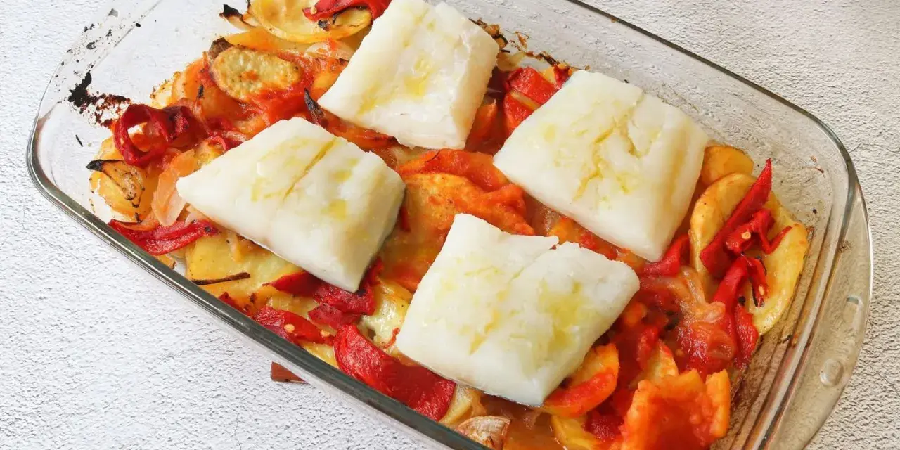 Cuatro porciones de bacalao al horno reposan sobre patatas y pimientos asados en una fuente de vidrio.