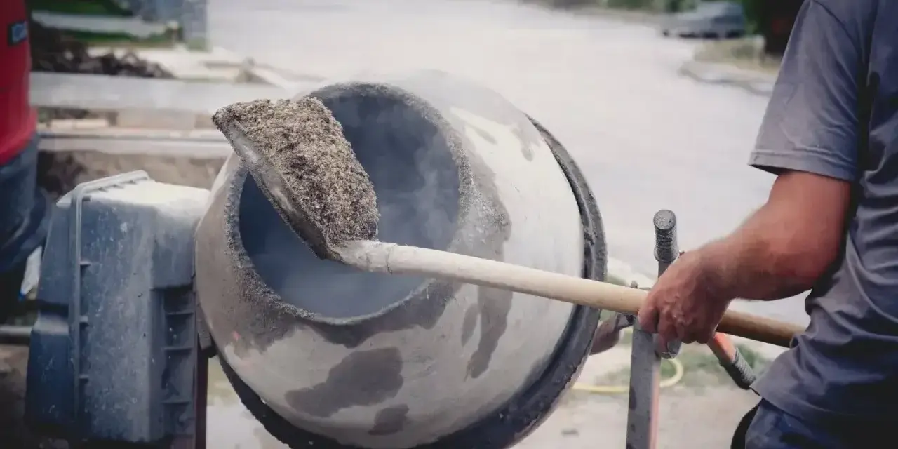Robotnik miesza łopatą mieszankę cementową w betoniarce.