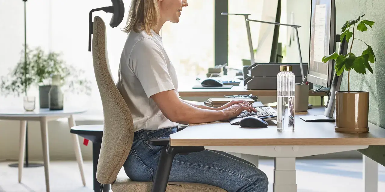 En kvinna sitter ergonomiskt vid ett skrivbord och arbetar vid datorn.