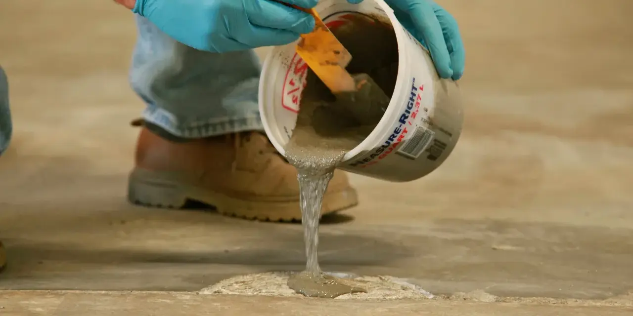 Man con guantes azules vierte hormigón líquido de un cubo para reparar el suelo. Aprende como hacer hormigón para suelo.