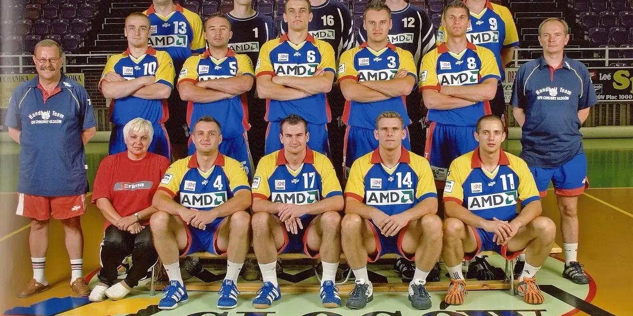 Drużyna SPR Chrobry Głogów pozuje do zdjęcia. Zawodnicy w żółto-niebieskich strojach sportowych, trenerzy i jedna kobieta.