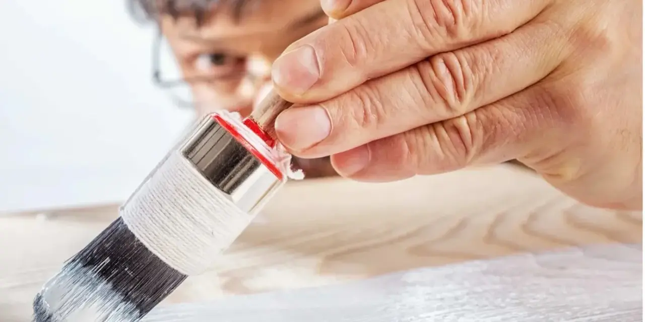 Un uomo applica il primer per legno con un pennello, preparando la superficie per la verniciatura.
