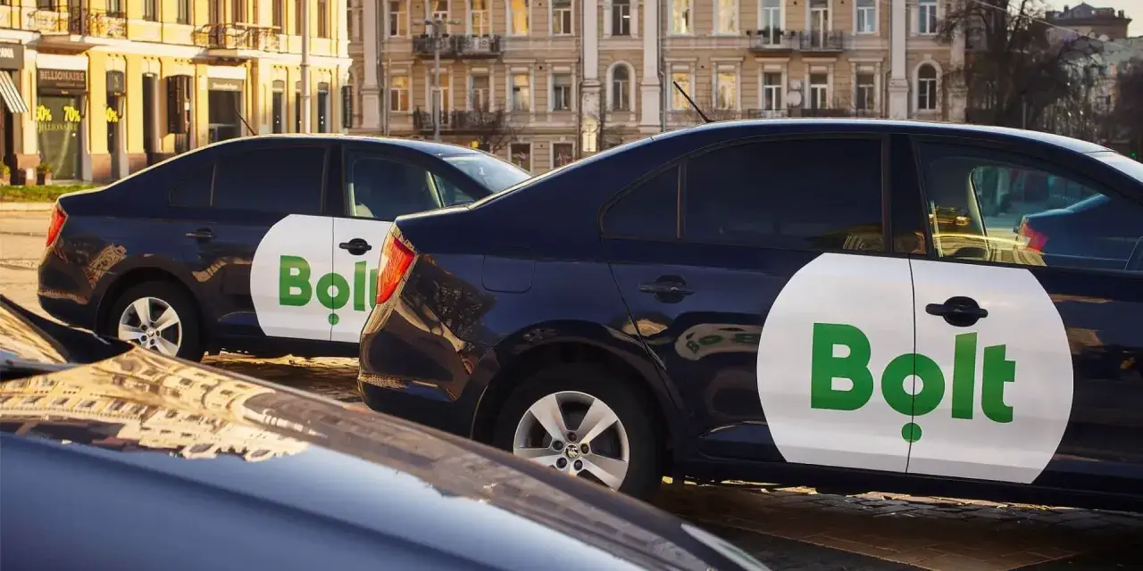 Ciemne samochody z logo Bolt, gotowe do pracy taxi bez licencji, stoją na ulicy.