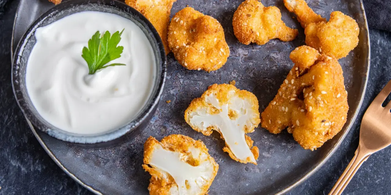 Knusprige Blumenkohl Nuggets aus dem Ofen, goldbraun paniert und mit Sesam bestreut, serviert mit einem cremigen Dip.