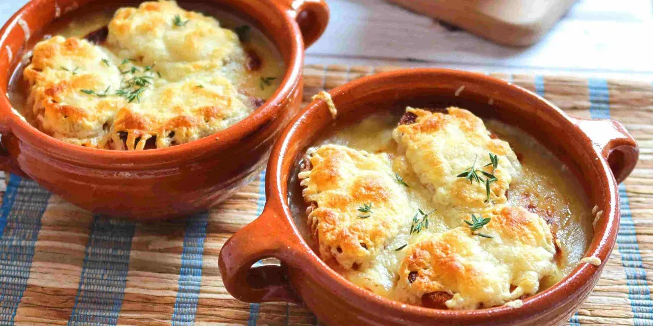 Dos cazuelas de barro con sopa de cebolla gratinada con queso y hierbas.