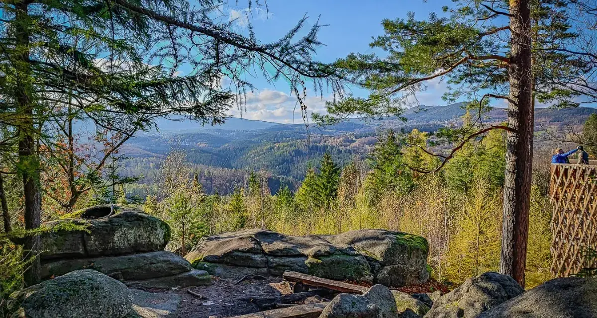 Kamienne skały i ławki na tle rozległej, leśnej panoramy Karkonoszy.