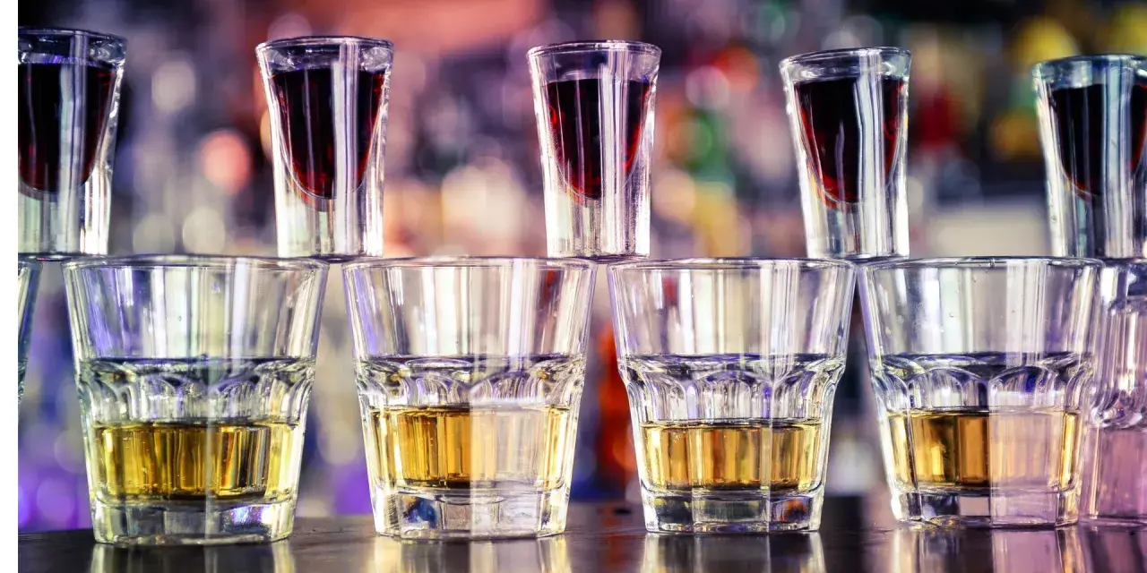 Rzędy kieliszków z bursztynowym alkoholem i ciemnoczerwonym likierem, gotowe do zrobienia jager bomb drink.