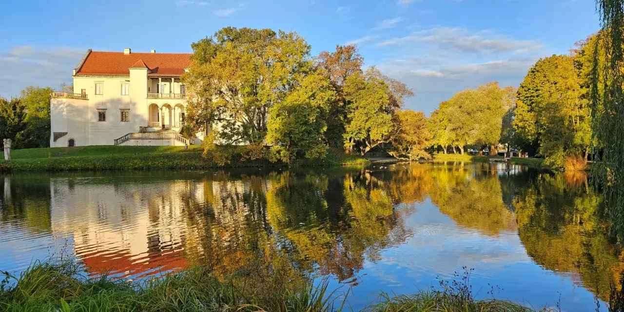 Zamek w Szydłowcu, otoczony jesiennym parkiem, odbija się w spokojnej tafli stawu. Idealne miejsce na zwiedzanie i podziwianie przyrody.