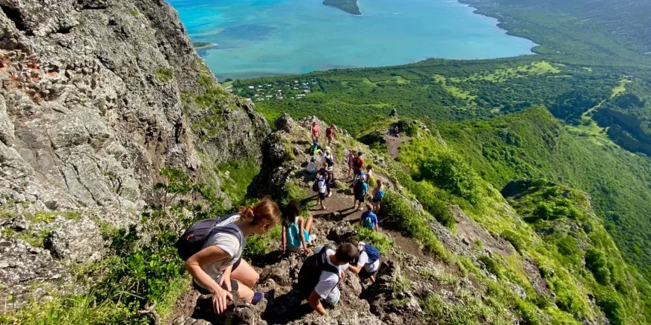 Grupa turystów wędruje po skalistym szlaku na Le Morne Mauritius, podziwiając zapierający dech w piersiach widok na turkusową lagunę i zielone wzgórza.
