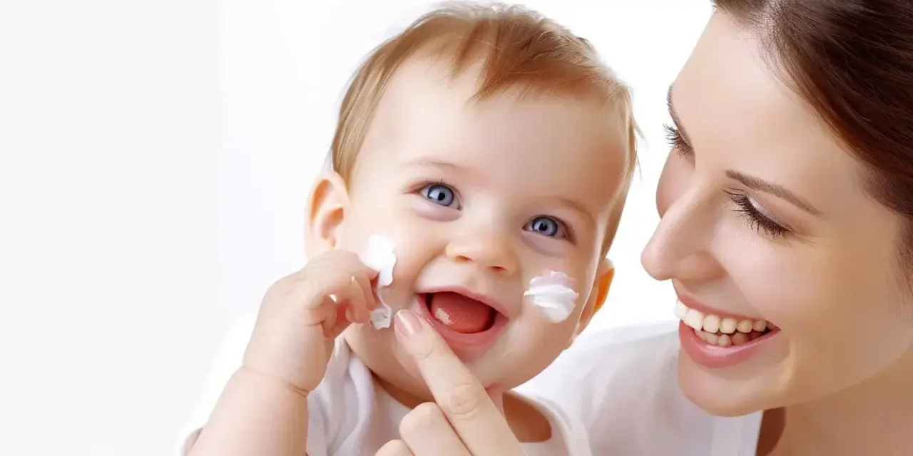 Uśmiechnięty maluch z białymi plamkami kremu na policzkach. Sudocrem na co? Na delikatną skórę dziecka, chroniąc ją i łagodząc.
