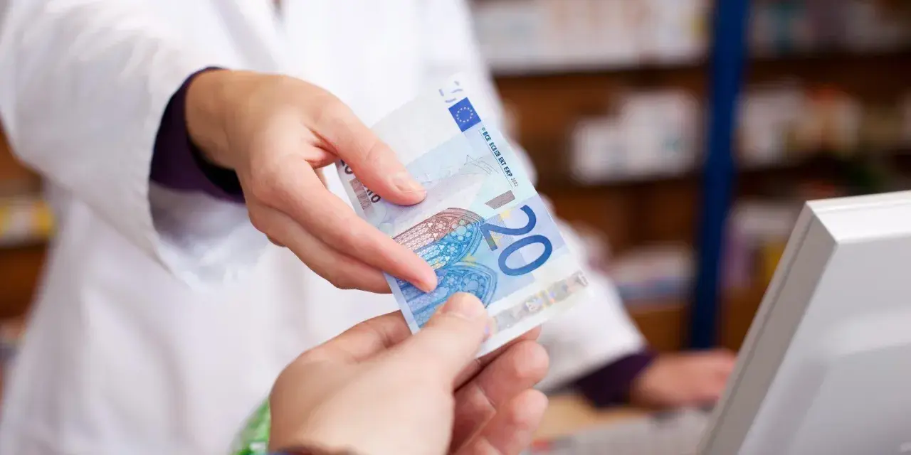 Eine Person in einem weißen Kittel reicht einen 20-Euro-Schein. Möglicherweise zur Bezahlung von Krankengymnastik Kosten.