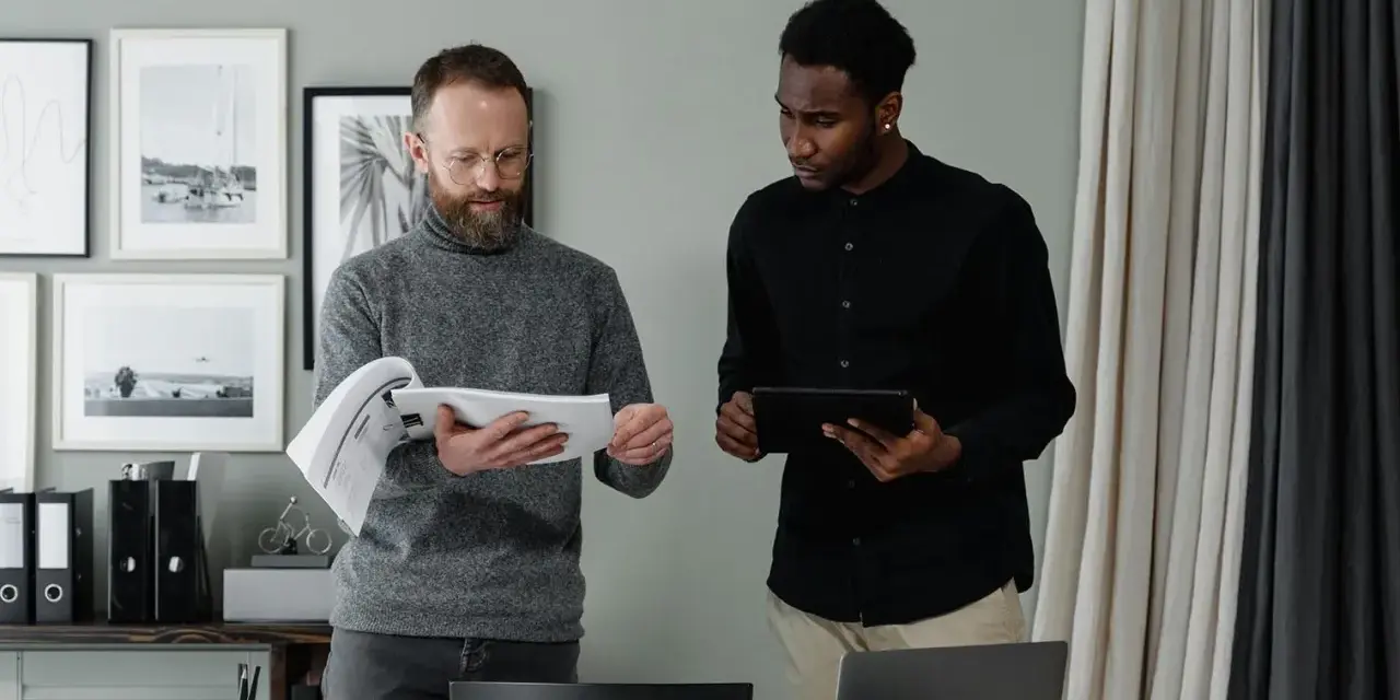 Two men review documents and a tablet, discussing the details of in-kind donation accounting.