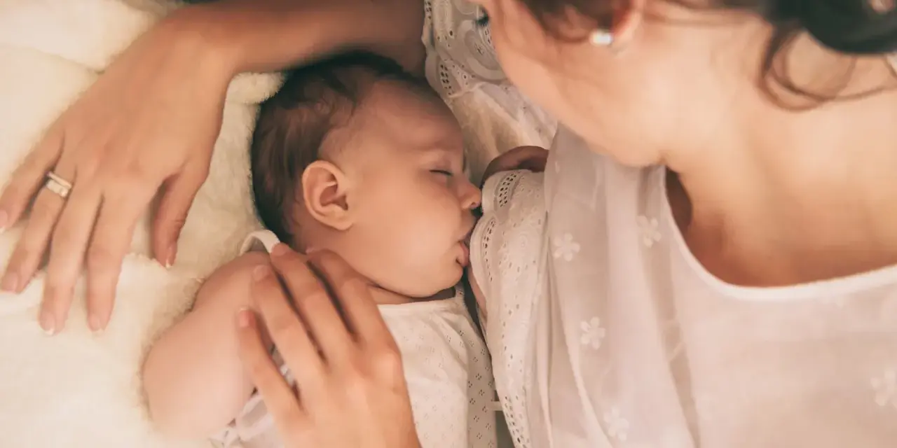Delikatne karmienie noworodka. Mama czule tuli dziecko, które śpi, ssąc pierś. Wskazówki, jak wybudzić noworodka do karmienia, mogą być pomocne w takich chwilach.