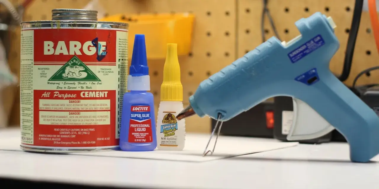 A hot glue gun, Barge cement, Loctite super glue, and Gorilla Super Glue are on a workbench. Does Gorilla Glue melt? This image shows various adhesives.