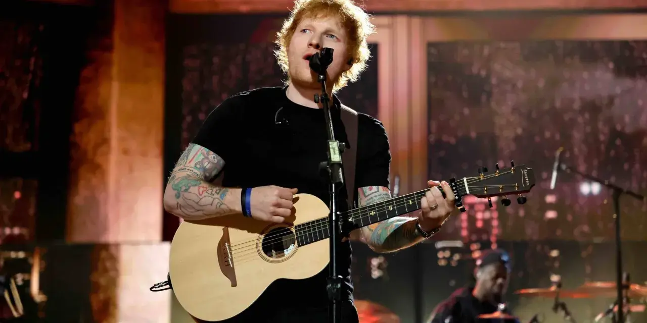 Ed Sheeran spielt Gitarre und singt auf einer Bühne.