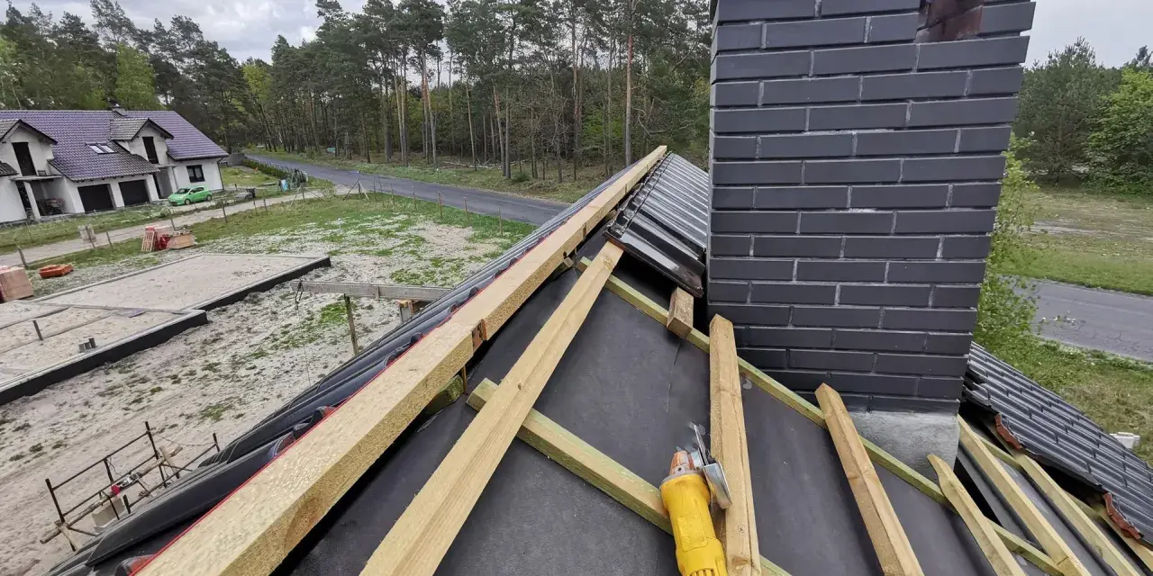 Budowa dachu: widok na drewniane łaty i komin. Wymiary kontrłaty są kluczowe dla stabilności konstrukcji.