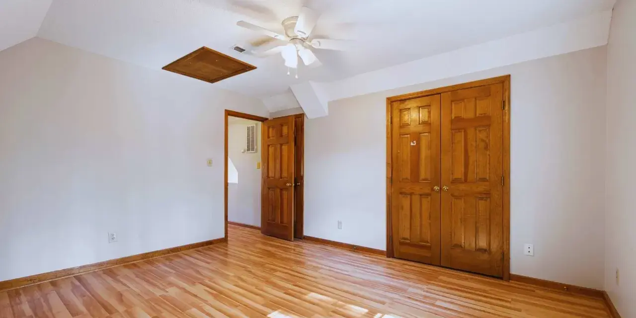 Habitación con suelo de madera clara y puertas de madera oscura, creando un bonito contraste. Un ventilador de techo ilumina el espacio.