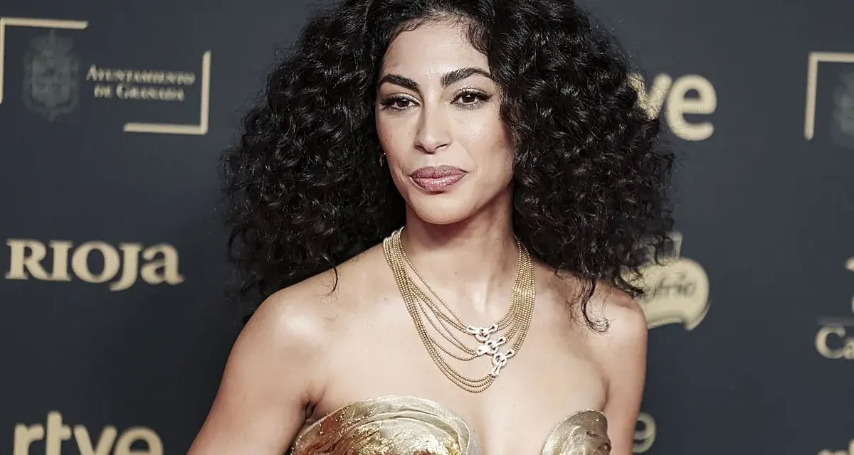 Mujer con espectacular pelo rizado, peinado con volumen y brillo. Luce un vestido dorado y un collar de cadenas.