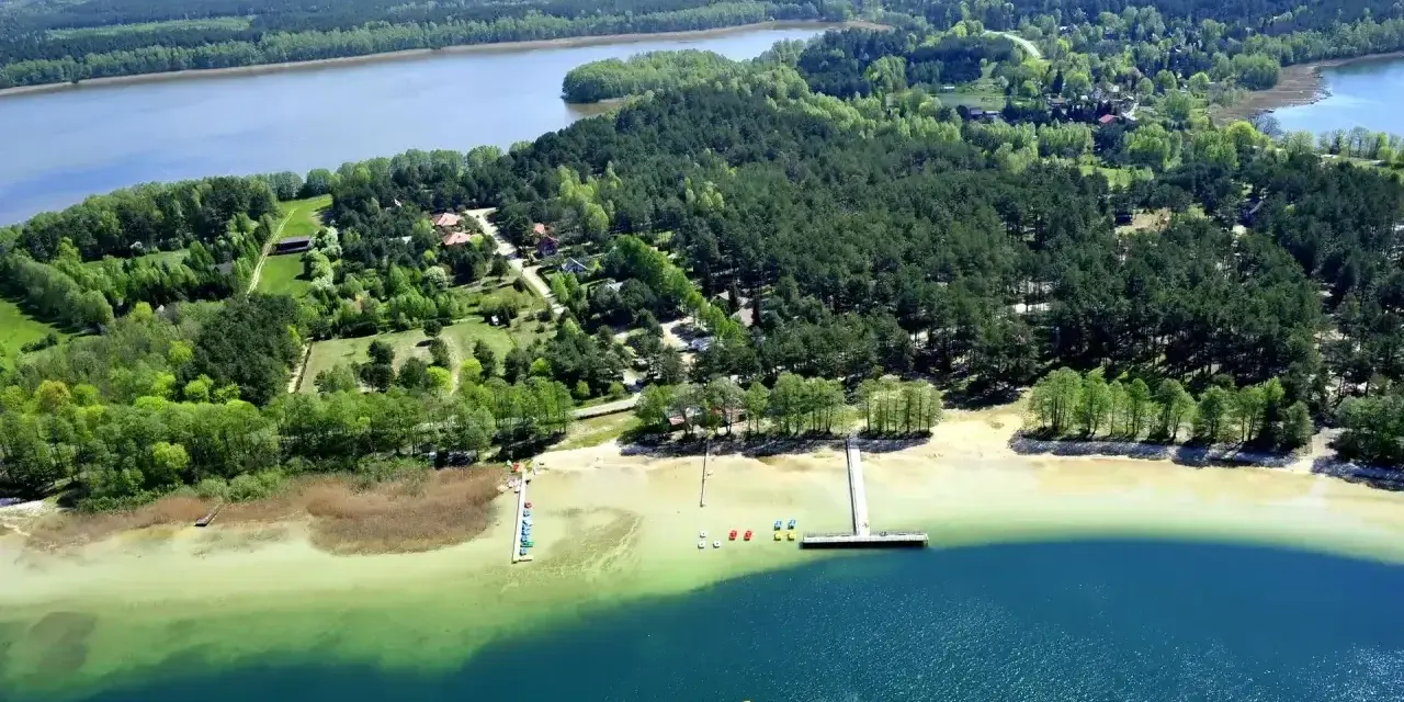 Malownicze warchały jezioro otoczone lasem, z piaszczystą plażą, pomostami i kolorowymi łódkami.