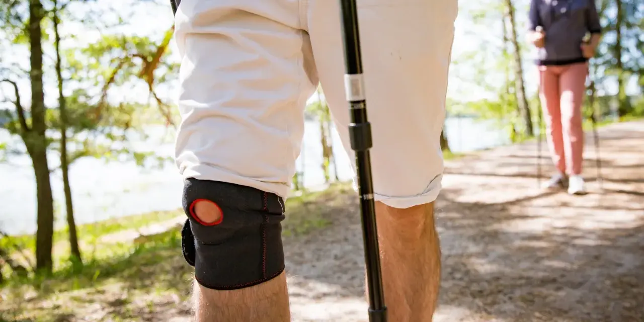 Mann mit Kniebandage beim Nordic Walking. Knieschmerzen beim Bergabgehen beeinträchtigen die Wanderung.