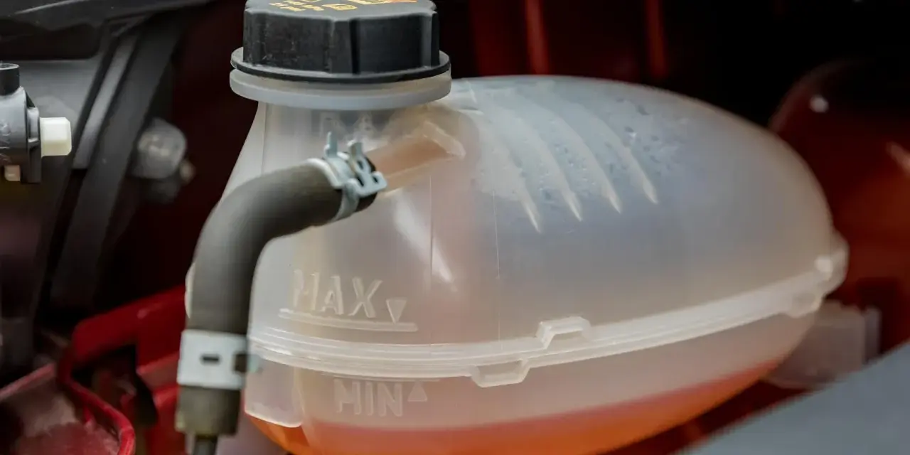 A car's coolant reservoir with MAX and MIN lines. The orange coolant is between the lines, indicating the correct level. This image helps answer "what coolant does my car need.