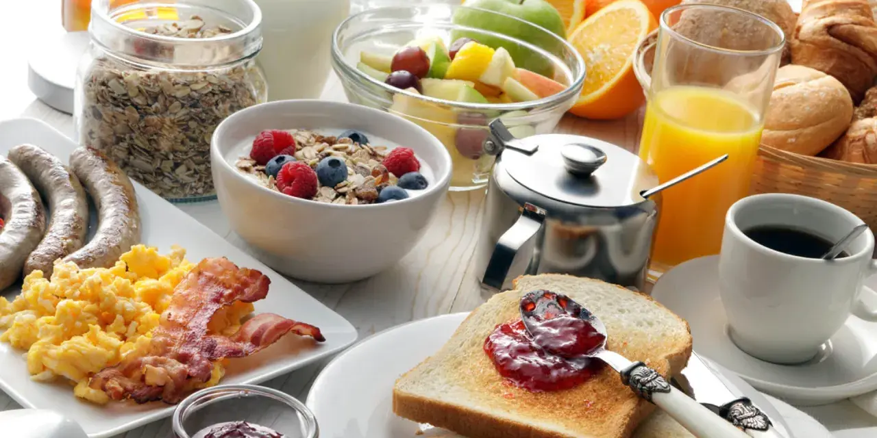 Deftiger Brunch in Schleswig-Holstein: Rührei, Speck, Würstchen, Müsli, Obst, Saft und Kaffee.