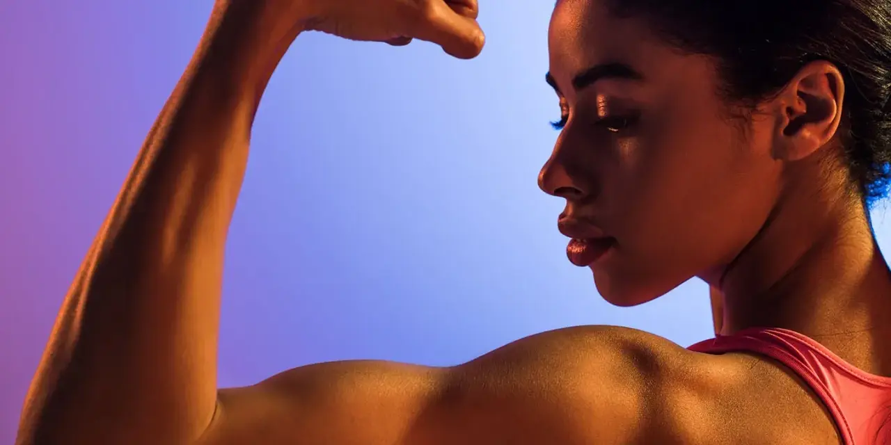 En kvinna flexar sin biceps, en demonstration av styrka och i muskelminnet.