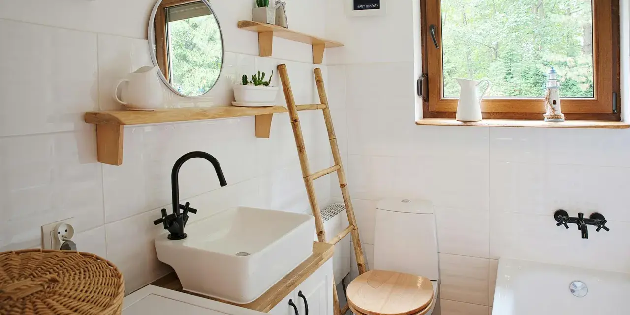 Bagno piccolo con piastrelle bianche lucide, lavabo squadrato, specchio rotondo e scala in bambù. Idee piastrelle bagno piccolo: la luminosità è la chiave.