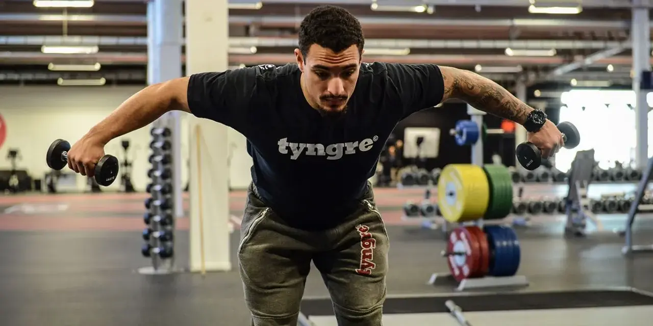 Man tränar baksida axlar med hantlar på gym.