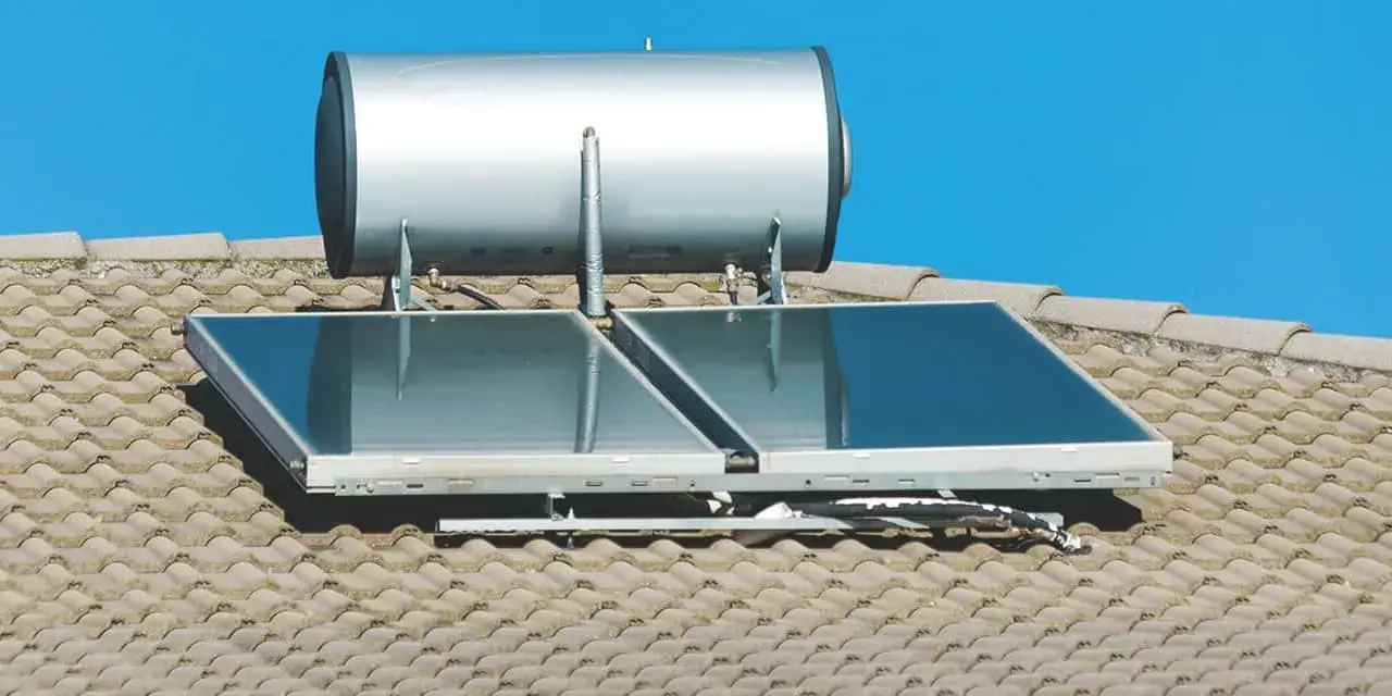 Ein pvt kollektor mit einem Warmwasserspeicher auf einem Ziegeldach unter blauem Himmel.