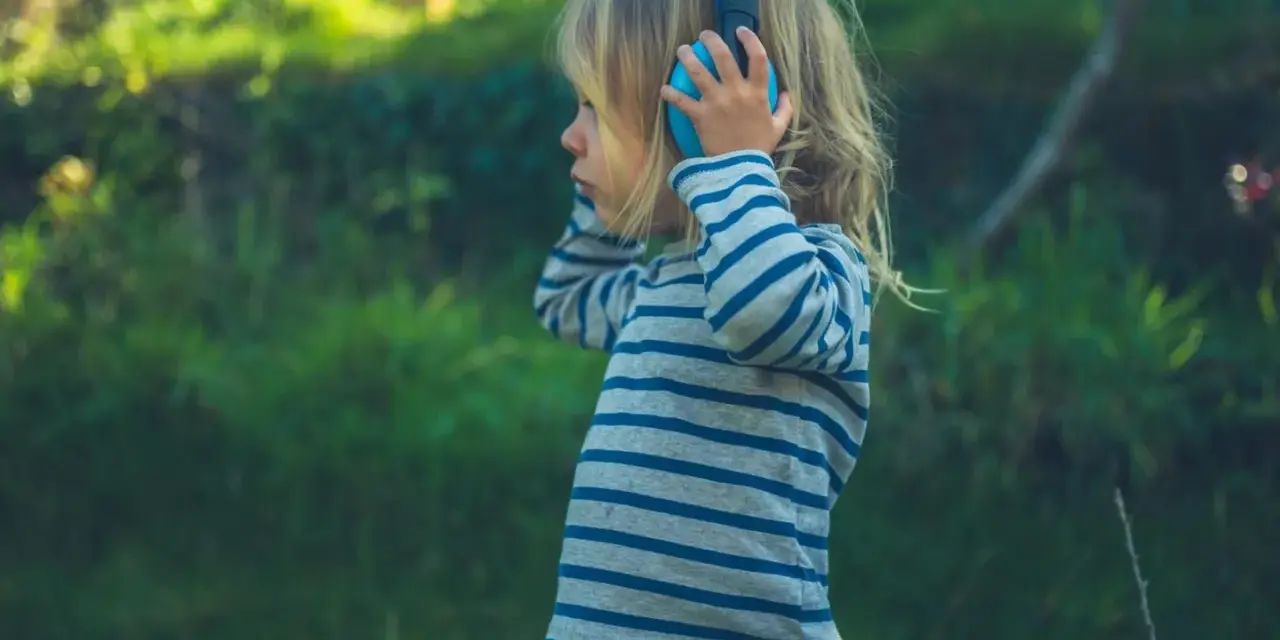 Ein Kind mit Kopfhörern im Freien, das die Welt der Klänge entdeckt. Diese Szene zeigt die Reizoffenheit bei Kindern, die sich neugierig auf neue Erfahrungen einlassen.