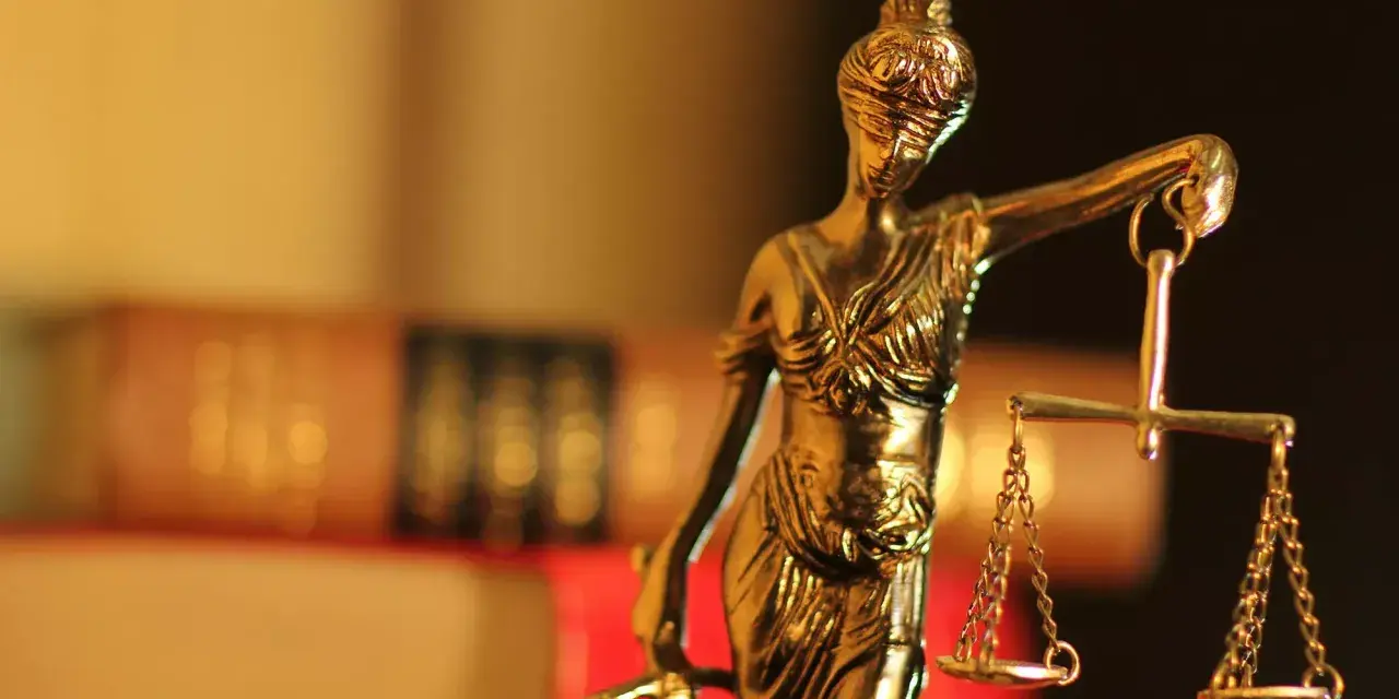 Justitia-Statue mit Waage und Schwert, symbolisiert Gerechtigkeit. Im Hintergrund unscharfe Bücher, die auf einen Fall mit 1/3 Betreuung hindeuten könnten.