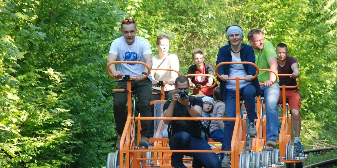 Rodzina na drezynach w Bieszczadach, ciesząca się zielenią i słońcem. Radość i wspólna przygoda na torach.