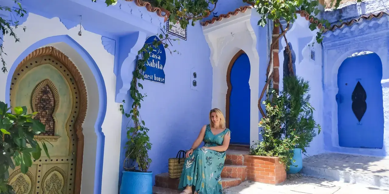 Maj w Maroku to idealna pogoda na zwiedzanie błękitnego miasta Chefchaouen. Kobieta w letniej sukience siedzi na schodach przed Casa Sabila.