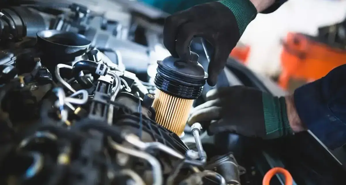 Mechanik w czarnych rękawiczkach dokonuje wymiany filtra paliwa w silniku samochodu.