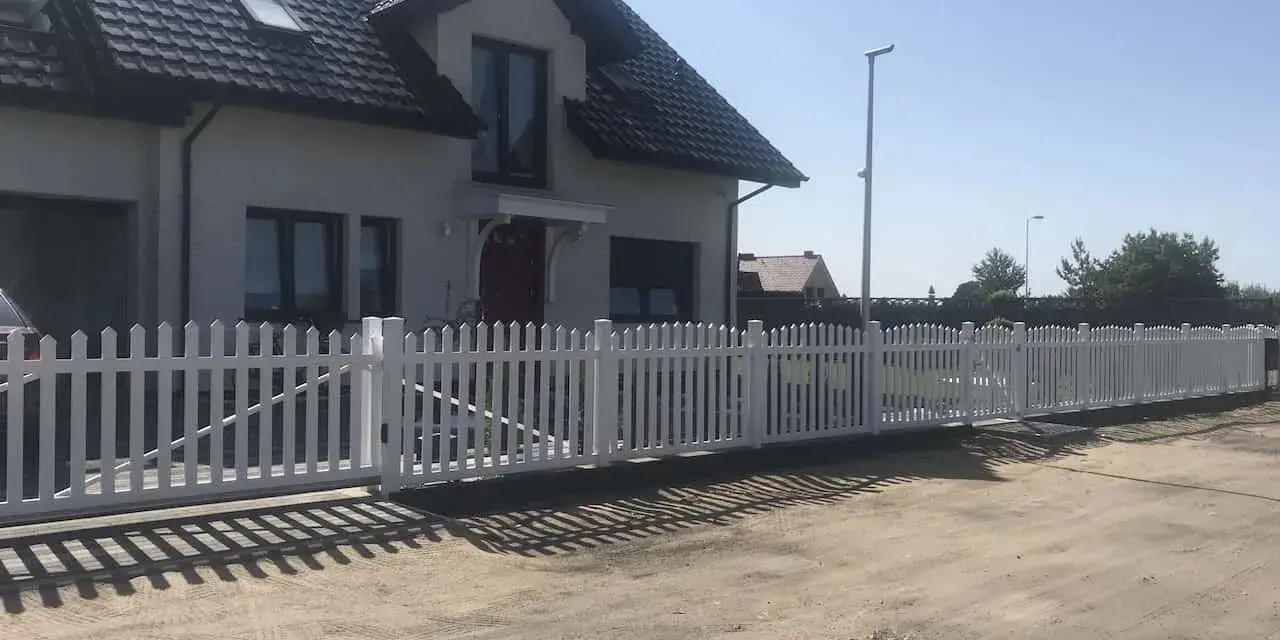 Biały płotek ogrodowy zrób to sam, idealnie otacza dom. Wygląda jak nowy, dodaje uroku posesji.