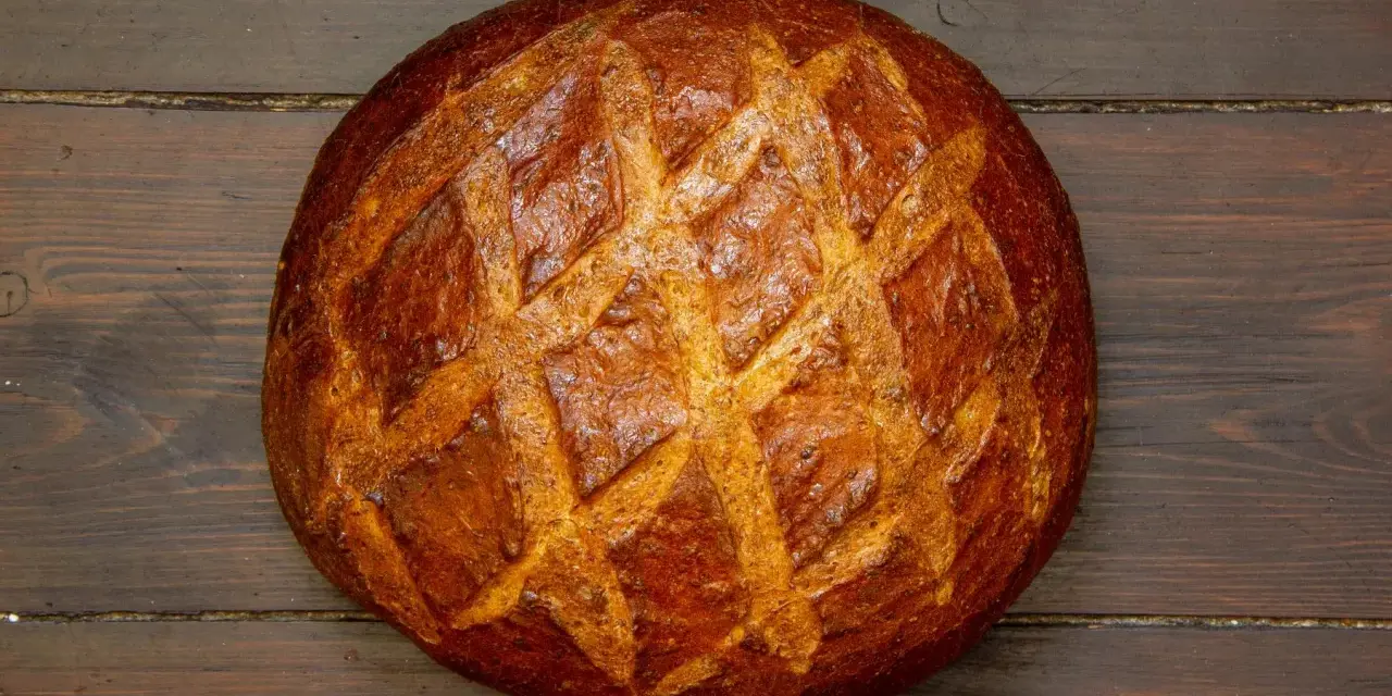 Ein **freigeschobenes Brot** mit knuspriger Kruste und Rautenmuster liegt auf dunklem Holz.