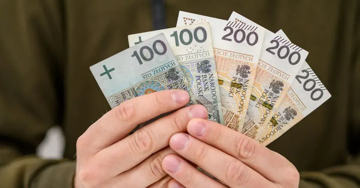 Dłonie trzymają polskie banknoty: 100 i 200 zł. To symbol nagrody za pracę, jak 800 plus tylko dla pracujących.