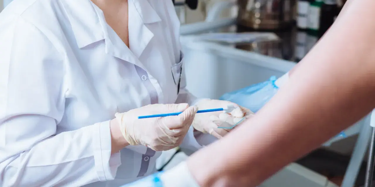 Lekarz w białym fartuchu i rękawiczkach trzyma szczoteczkę do cytologii płynnej nad szkiełkiem.
