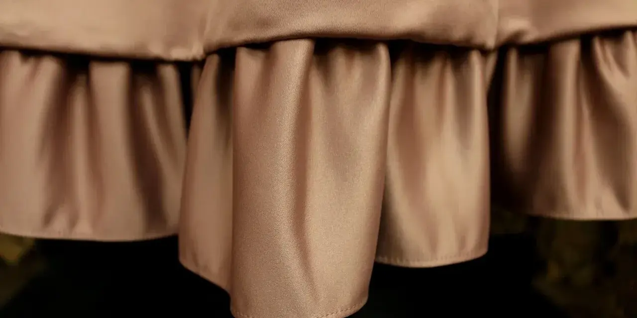 Delikatne marszczenia na **satynowym** materiale tworzą efektowną falbanę, dodając elegancji.