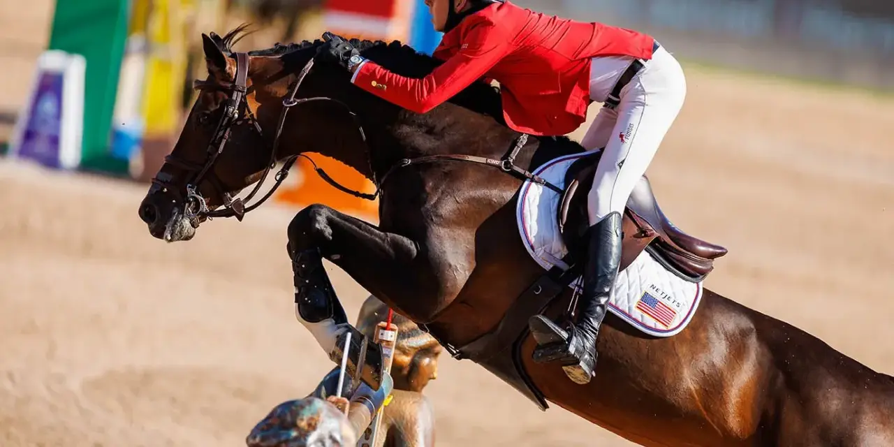 Le cheval Balou du Reventon saute un obstacle, son cavalier en veste rouge le guidant avec précision.