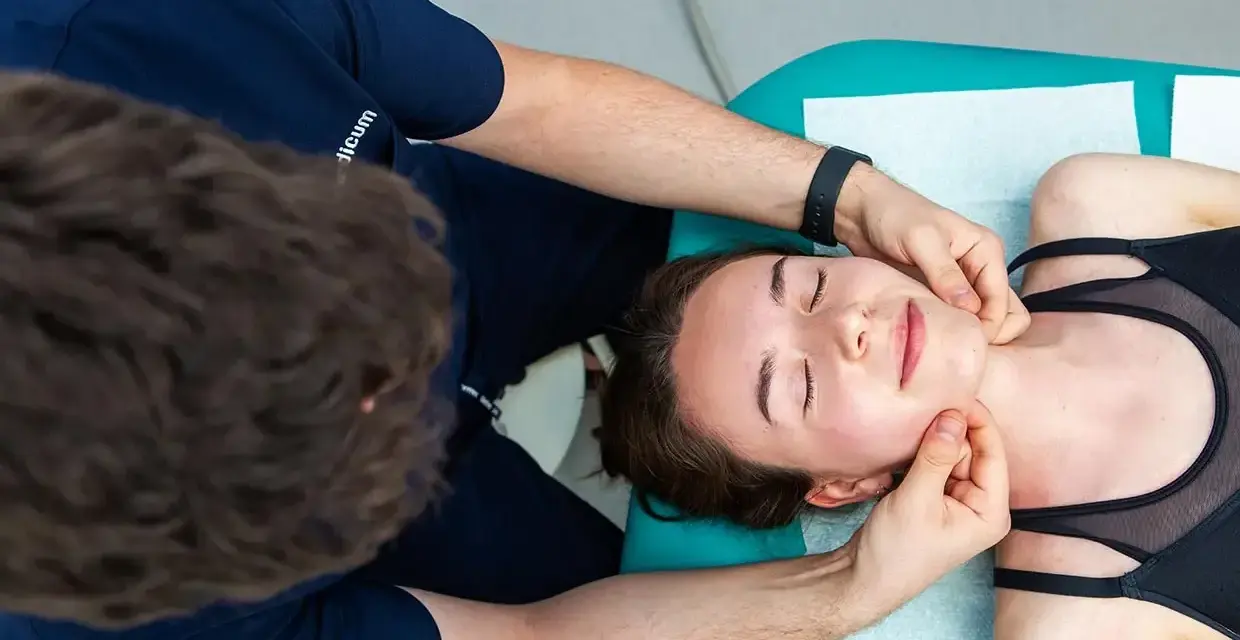 Fizjoterapeuta wykonuje zabieg fizjoterapii stomatologicznej, delikatnie masując twarz pacjentki.