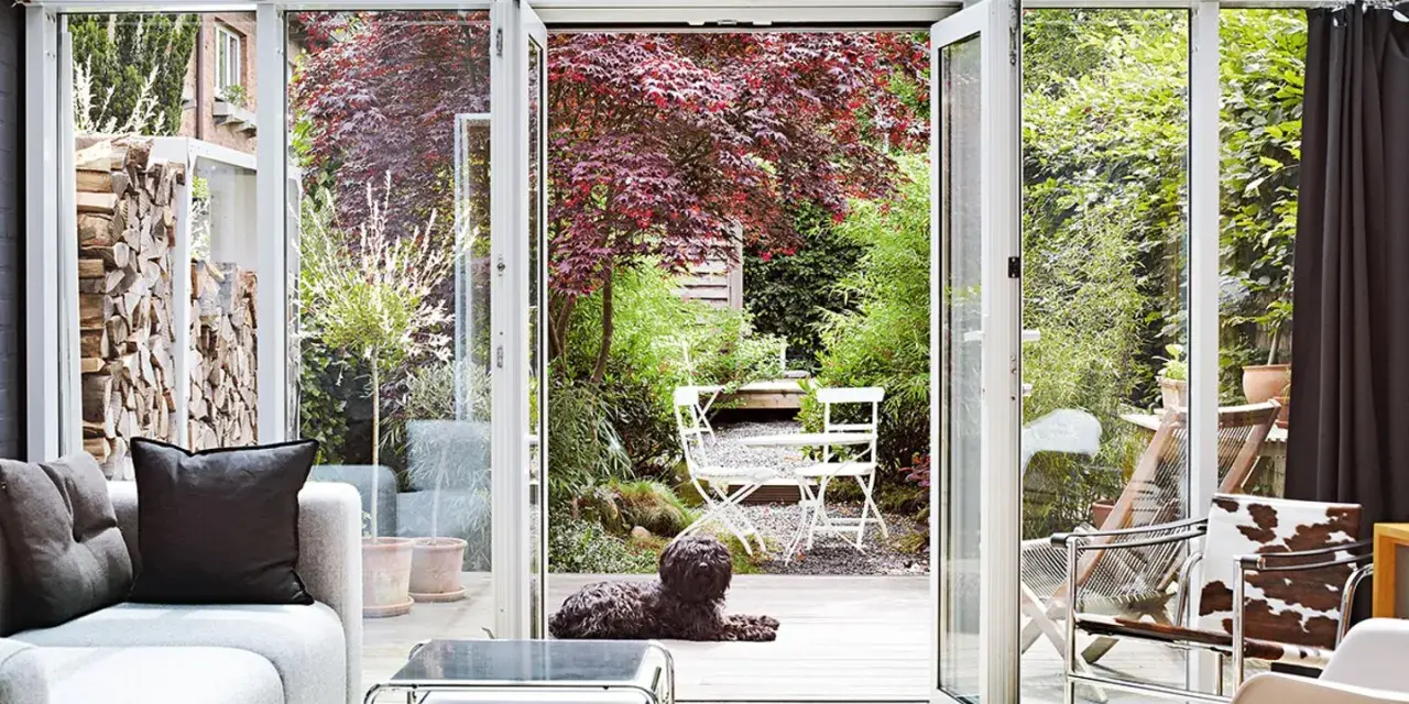 Gemütliches Wohnzimmer mit Blick in den Garten. Ein Hund liegt auf der Holzterrasse, ideal zum Wintergarten einrichten.
