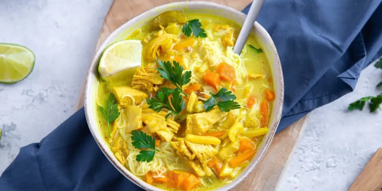 Aromatyczna zupa z kurczakiem, makaronem i warzywami, ozdobiona natką pietruszki i ćwiartką limonki.
