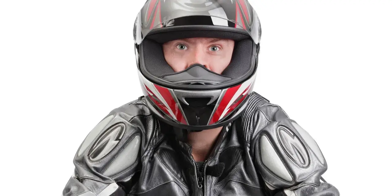 Occhi spalancati dietro un casco stretto, pronto per la corsa. La tuta in pelle grigia e nera completa il look da motociclista.