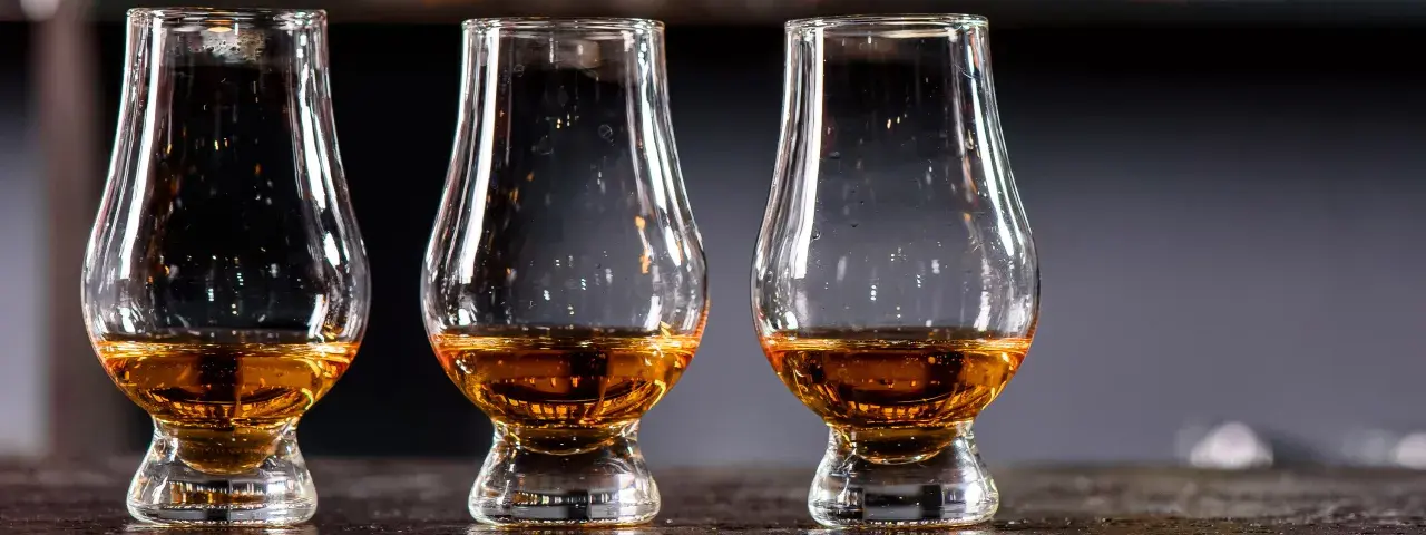 Drei Gläser mit bernsteinfarbenem Whisky stehen nebeneinander. Ein Blick auf die Whisky Kalorien für Genießer.
