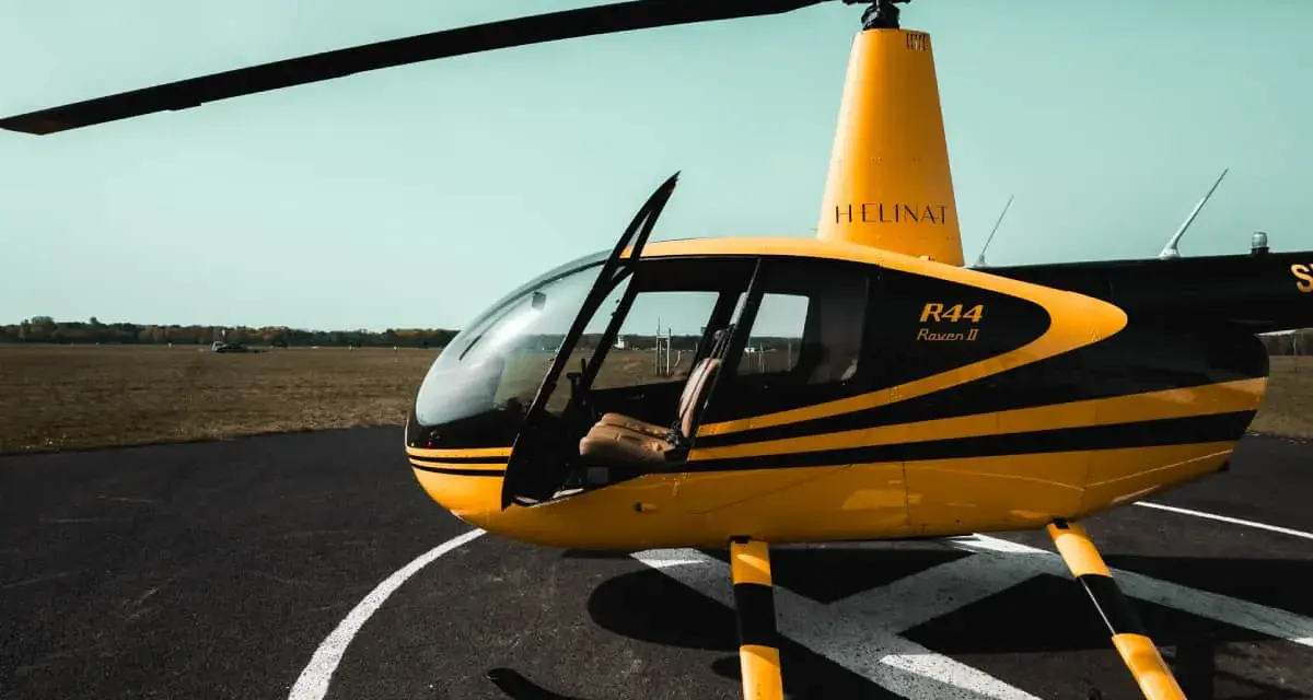 Żółto-czarny helikopter Robinson R44 Raven II na płycie lotniska. Marzysz, jak zostać pilotem helikoptera?